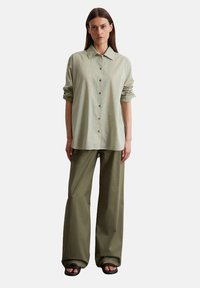 Light green button-up shirt with a pointed collar and rolled sleeves. Olive green wide-leg pants and black sandals complete the outfit.