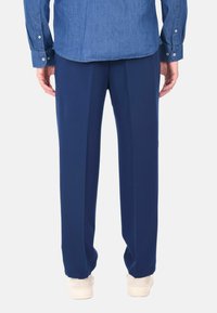 Pantaloni blu navy su misura con una texture liscia, caratterizzati da una taglio dritto e pieghe, abbinati a una camicia in denim.