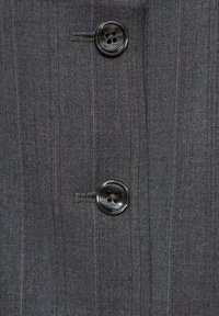 Tissu gris foncé avec de subtiles rayures verticales et deux boutons noirs à quatre trous cousus près du centre.