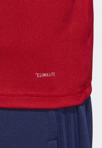 Chemise en tissu texturé rouge avec un bas bleu marine. Présente une étiquette visible « CLIMALITE » près de l'ourlet, indiquant une technologie d'évacuation de l'humidité.
