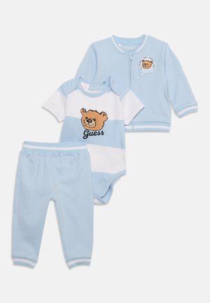 Ensemble de vêtements pour bébé bleu clair avec pantalon, body rayé avec un ours en peluche et le texte "Guess", et une veste zippée avec un patch ours en peluche.