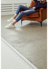 Bílé tenisky, roztrhané modré džíny a námořnický svetr, nošené při sezení na oranžovém křesle. Betonová podlaha s texturovaným odtokovým páskem.