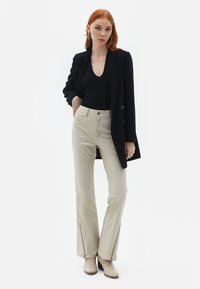 Sort v-hals top, marineblå blazer og beige bukser med sidelukninger. Skoene er lysebrune ankelstøvler. Enkelt, figursyet design med neutrale farver.