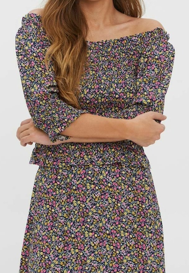 Haut fleuri à épaules dénudées avec manches trois-quarts, arborant un design smocké en noir, orné de petites fleurs multicolores.