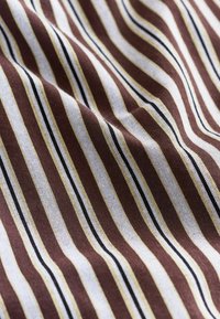 Tkanina w paski w odcieniach brązu, bieli i żółci, z czarnymi akcentami. Materiał wydaje się miękki o teksturowanej powierzchni.