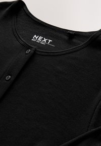 Black ribbed cardigan with a round neckline, featuring a buttoned front closure and a soft texture. Brand label reads "NEXT."