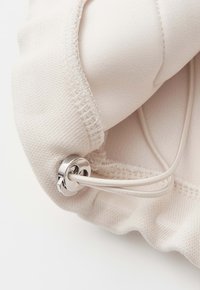 Primo piano di tessuto beige con fermacorda regolabile in argento e coulisse elastica, che mette in risalto la trama e i dettagli delle cuciture.