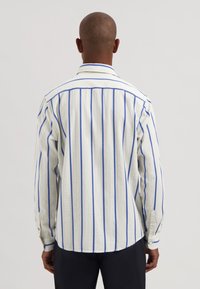 Gestreiftes Langarmhemd in Weiß und Blau mit strukturierter Stoffqualität, einem geknöpften Kragen und Knöpfen an den Manschetten. Taillierte Passform, geschwungener Saum.