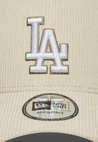 Beige ribfluwelen pet met een geborduurd "LA" logo in wit met gouden accenten, verstelbare band met New Era branding aan de binnenzijde.