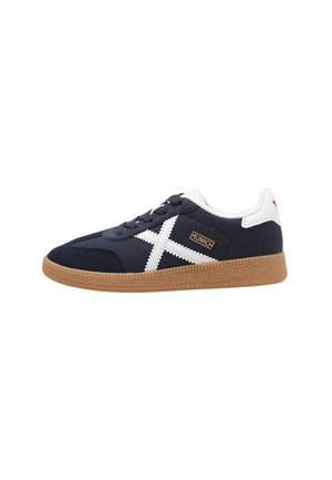 Zapatilla de lona color marino con acentos blancos, que cuenta con una suela de goma texturada, punta redondeada y un detalle del logo dorado en el lateral.