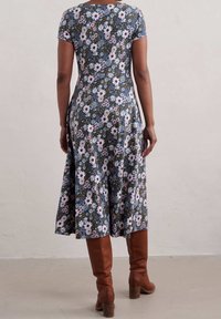 Květinové šaty po kolena s krátkým rukávem, s námořnicky modrým pozadím a růžovými a bílými květy. Spárované s hnědými kozačkami po kolena.