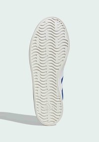 Sula av en sneaker med en vågig textur, övervägande vit med blå accenter och präglad logotypdetalj vid hälen.