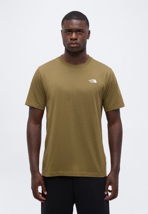 Mand iført en olivengrøn The North Face t-shirt med korte ærmer og sorte bukser, stående mod en ensfarvet hvid baggrund.