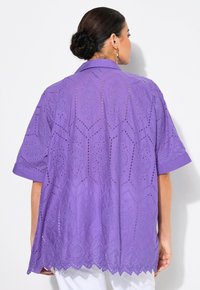 Top viola a maniche corte con intricati motivi a taglio, orlo scallop e vestibilità rilassata, realizzato in tessuto leggero.