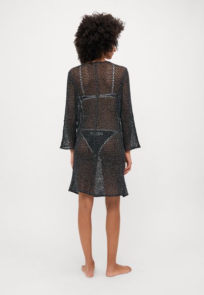 Vestido de punto negro con mangas largas, un diseño de tejido abierto y una longitud hasta la mitad del muslo con un dobladillo curvado. Textura suave y silueta ajustada.