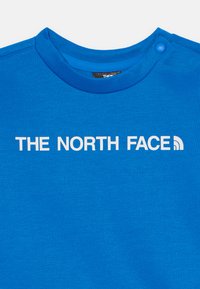 Φωτεινό μπλε φούτερ με στρογγυλή λαιμόκοψη, απαλή υφή και λευκό εκτυπωμένο λογότυπο "THE NORTH FACE" με μια απλή καμπύλη λεπτομέρεια.