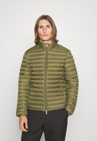 Olijfgroene pufferjack met gestikte textuur, rits voorkant, hoge kraag en contrasterende oranje ritstrekkertje. Slanke pasvorm met lange mouwen.