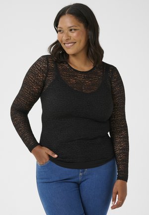 Top nero a maniche lunghe con motivo in pizzo testurizzato, scollatura rotonda, design a strati, indossato sopra una base nera aderente. Abbinato a jeans blu.