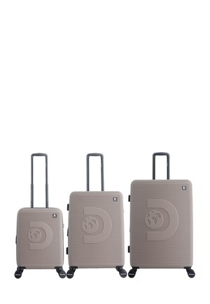 Three beige hard-shell suitcases of small, medium, and large sizes with extended black handles, front logo, and four spinner wheels each.