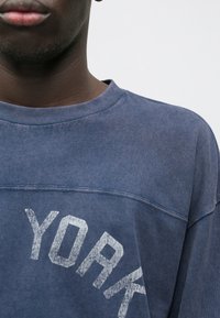 Modrá mikina vyrobená z bavlny, s okrúhlym výstrihom a vyblednutou grafikou "YORK" na prednej strane. Mäkka textúra s voľným strihom.