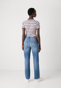 Stripet skjorte med korte ermer i hvit og burgunder, kombinert med lyseblå straight-leg jeans. Merkbar lærpatch på baksiden av jeansens midje.