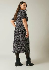 Svart blommig klänning med korta ärmar, med figurnära midja och en flödande nederdel. Matchad med svarta ankelskoter. Texturerad tyg med små lila blommor.