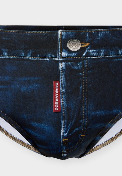 Sous-vêtements pour hommes stylisés avec un imprimé en denim bleu, des coutures jaunes, un bouton en métal et une étiquette rouge portant l'inscription "DSQUARED2" à l'avant.