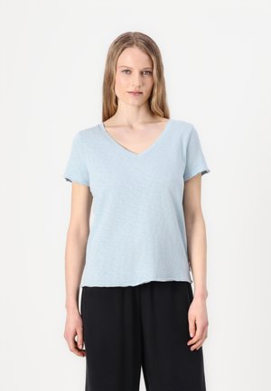 T-shirt azzurro chiaro a scollo a V realizzato in un tessuto morbido e testurizzato. Maniche corte e vestibilità rilassata, l'orlo arriva alla vita, abbinato a pantaloni neri.
