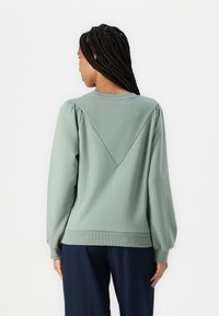 Sudadera de algodón verde con una costura trasera triangular y mangas abullonadas. Los puños y el dobladillo de canalé completan el diseño relajado y casual.