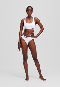 White sports bra and matching bikini bottom with a logo band in black. Smooth, stretchy fabric. Simple design with minimal detailing.