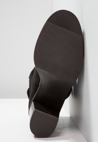 Botín alto de ante negro con suela de goma texturizada, con puntera redondeada y logo mínimo en la superficie de la suela.