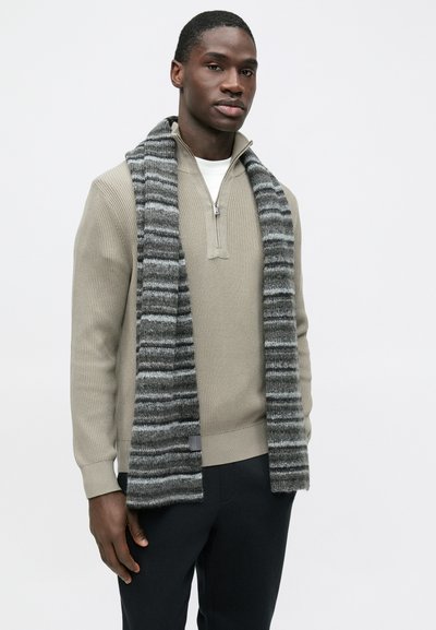 Pull en tricot beige clair avec un col zippé, associé à une longue écharpe en laine rayée gris et noir. Texture lisse, coupe ajustée.