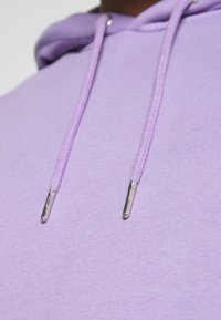 Felpa viola con una texture morbida. Presenta punte metalliche argento sui lacci e una vestibilità comoda e rilassata.