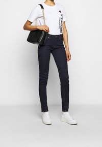 Vit t-shirt med röd hjärt-grafik och svart text, mörkblå skinny jeans och vita sneakers. Svart kviltad handväska med kedjeslinga.