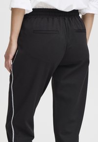 Musta collegehousut joustavalla vyötärönauhalla, kahdella takataskulla ja valkoisilla sivuraidoilla ulkosaumoissa. Pehmeä kangaspinta.