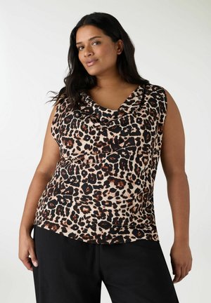 Donna che indossa una canotta senza maniche con stampa leopardata e scollo drappeggiato, e pantaloni neri, in piedi davanti a uno sfondo bianco semplice.