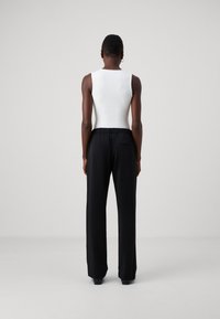 Vit ärmlös bodysuit i kombination med svarta, löst sittande byxor; elastisk midja och smidig tygtextur.