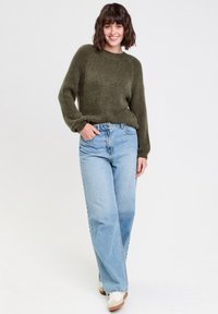 Pull en tricot vert olive oversize avec col rond, associé à un jean taille haute à jambes larges bleu clair et des baskets blanches.