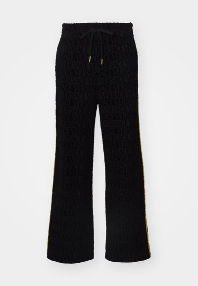 Pantalons noirs avec un tissu texturé arborant le motif du logo "VERSACE", une taille à cordon de serrage et des accents jaunes sur les côtés. Conception à jambes évasées.