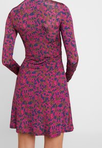 Sukienka z długim rękawem z kwiatowym wzorem w kolorze różowym, fioletowym i zielonym na granatowym tle. Fason posiada dopasowaną talię i rozkloszowany dół.