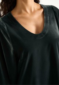 Sort fløjlstop med en v-halsudskæring, der har en glat tekstur og drapering. Stoffet har en subtil glans, der fremhæver det elegante design.