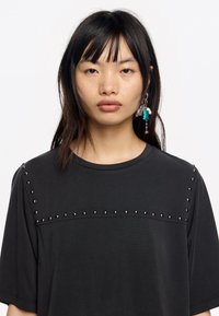 Czarny t-shirt z krótkimi rękawami i ozdobnymi srebrnymi ćwiekami na ramionach oraz klatce piersiowej. Miękka tkanina z okrągłym dekoltem.