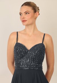 Abito grigio scuro con scollatura a V e spalline sottili. Il corpetto presenta paillettes decorative in un motivo ondulato, accompagnato da una gonna fluida.
