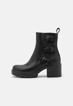 Stivale alla caviglia in pelle nera con tre cinturini e fibbie, tacco spesso e suola texturizzata. Finitura liscia con linguetta sul retro.