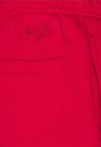 Rote Fleece-Jogginghosen verfügen über einen elastischen Bund, eine Seitentasche und ein deutlich gesticktes Logo in dunkler roter Faden.