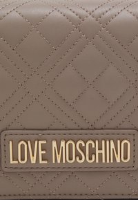 Prošívaná béžová kožená peněženka s pozlacenou destičkou s logem "LOVE MOSCHINO" a kontrastním prošíváním. Kompaktní obdélníkový tvar.