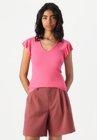 Haut rose à col en V côtelé avec des manches courtes volantes, assorti à un short marron ample de longueur mi-cuisse en tissu texturé.