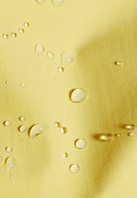 Σταγόνες νερού διάσπαρτες πάνω σε κίτρινο υλικό με υφή και ορατό σχέδιο ύφανσης, υπογραμμίζοντας την αντοχή στο νερό.