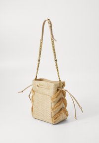 Beige geweven emmer tas met gouden kettinghengsel en getextureerde franjes in chevronpatronen aan de zijkanten, met lederen trekkoordsluiting en zak.