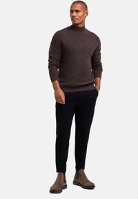 Brauner, gerippter Rollkragenpullover in entspannter Passform, kombiniert mit schwarzen, schmal zulaufenden Hosen und passenden braunen Stiefeletten. Glatte Textur und modernes Design.